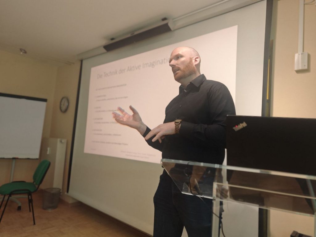 Benjamin Lang steht während des Workshops vor einer PowerPoint-Präsentation und erklärt die Aktive Imagination.